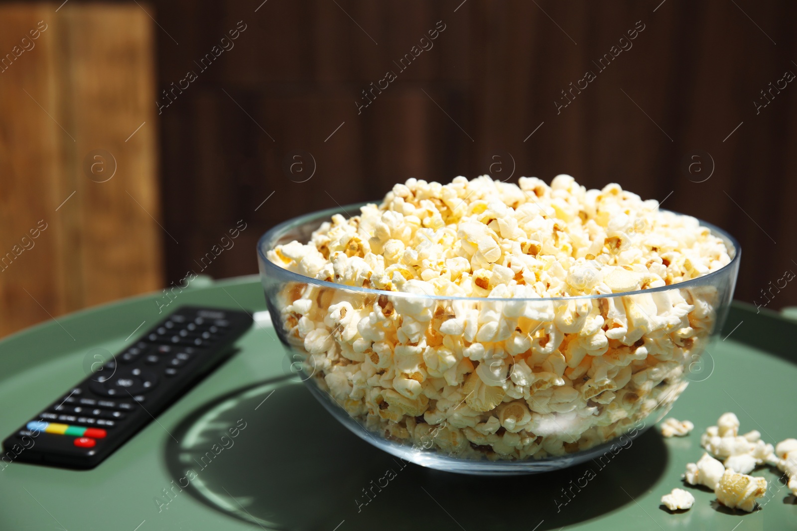 Photo of Bowl of popcorn and TV remote on table against blurred background. Watching cinema