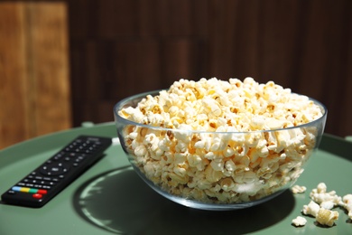 Photo of Bowl of popcorn and TV remote on table against blurred background. Watching cinema