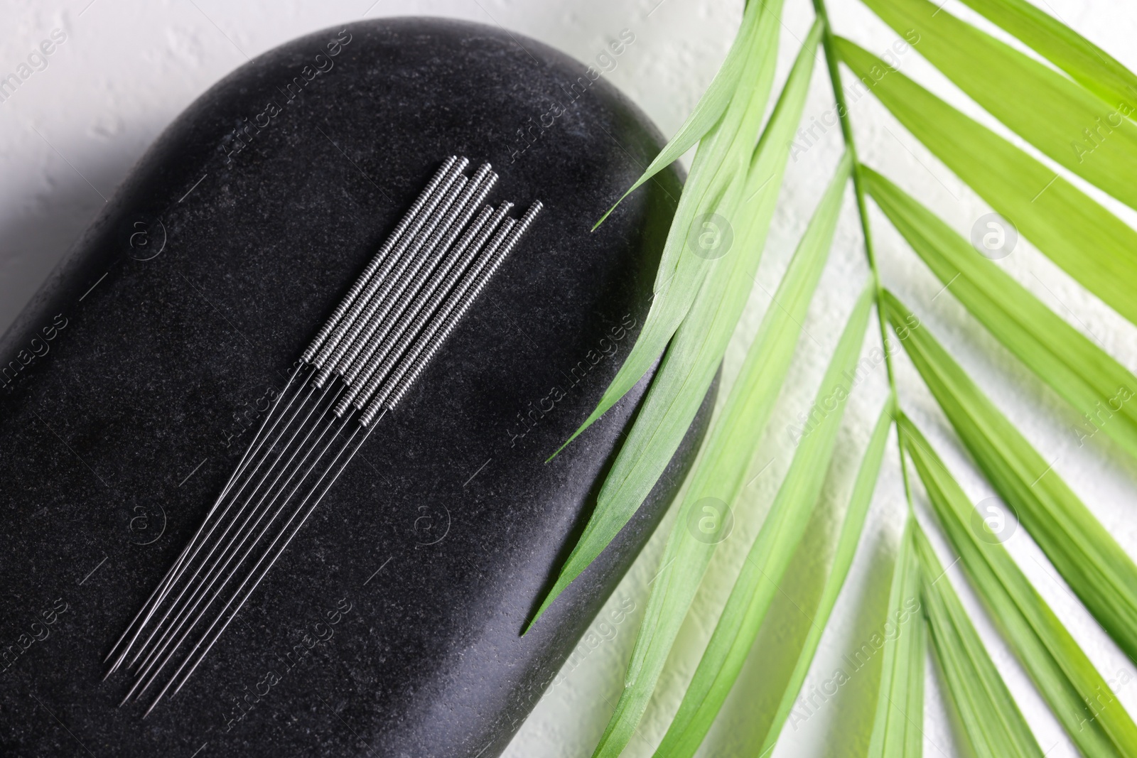 Photo of Acupuncture needles, spa stone and green leaf on white table, flat lay