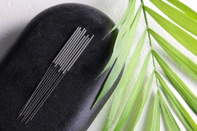 Photo of Acupuncture needles, spa stone and green leaf on white table, flat lay