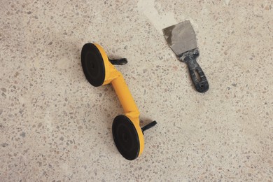 Photo of Glass suction plate and metal spatula on floor, above view. Tiles installation process