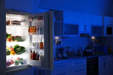 Stylish kitchen interior with refrigerator full of products at night