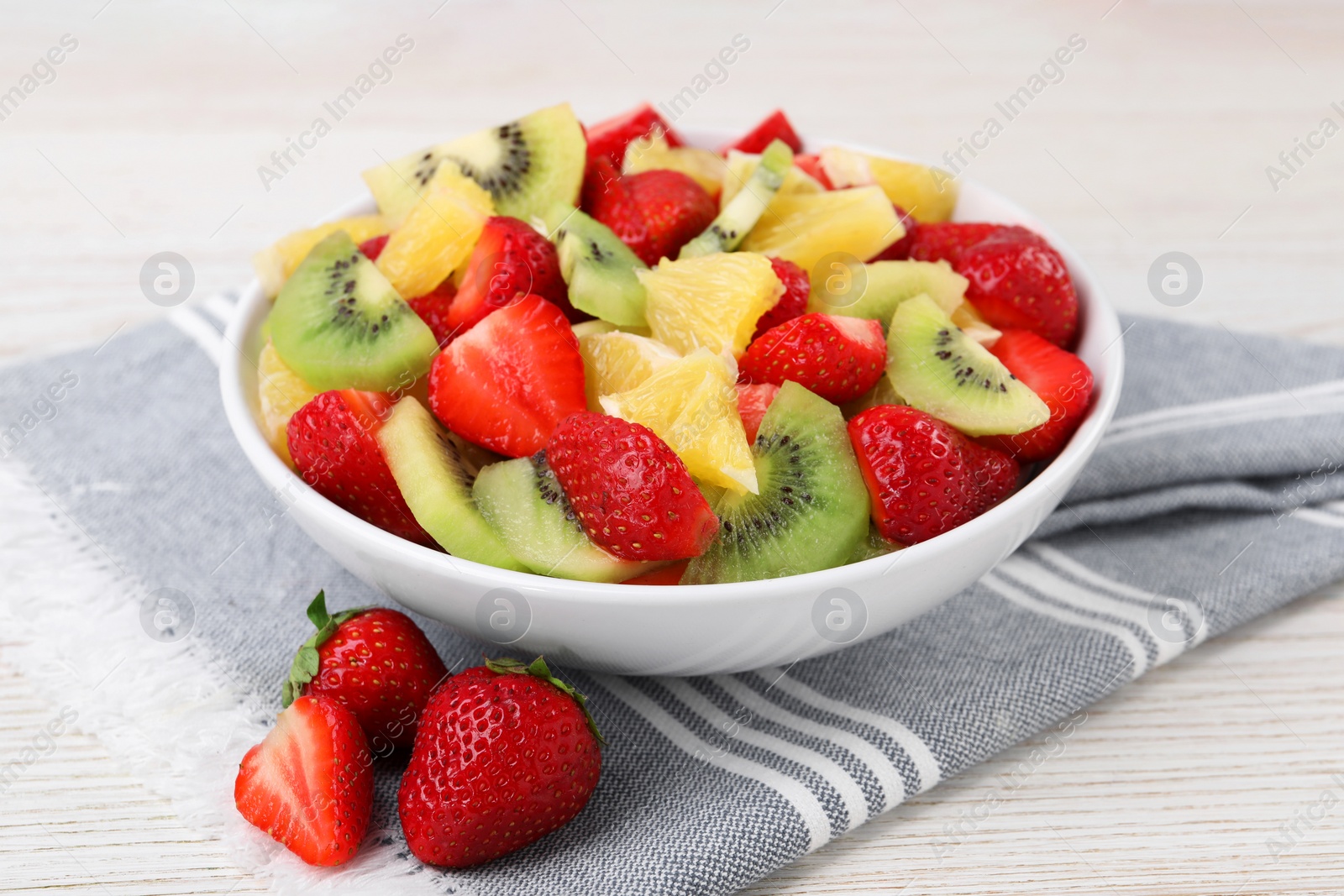 Photo of Delicious fresh fruit salad in bowl on white wooden table, closeup