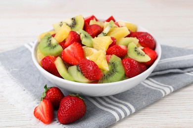 Delicious fresh fruit salad in bowl on white wooden table, closeup