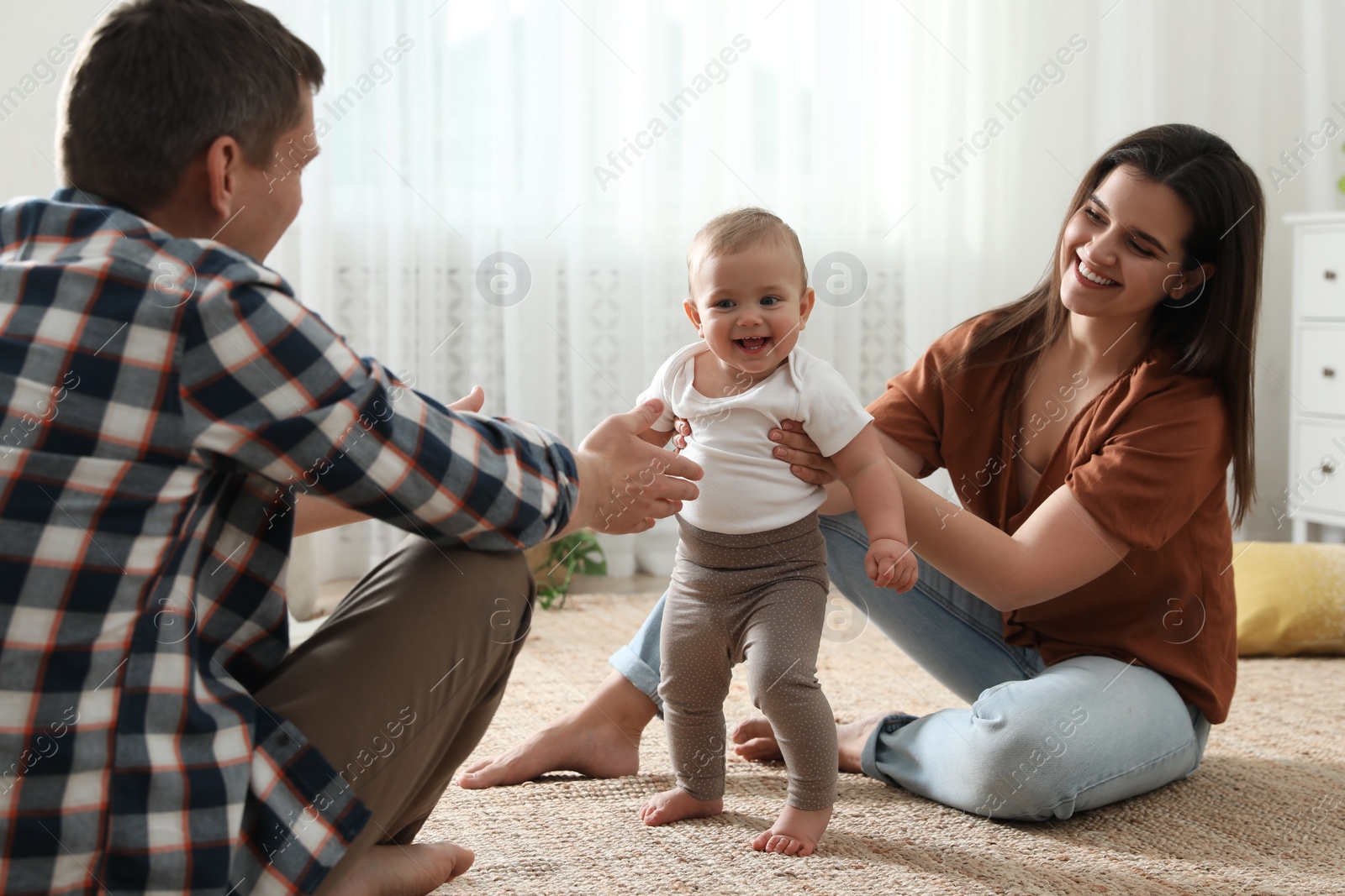 Photo of Parents supporting their baby daughter while she learning to walk at home