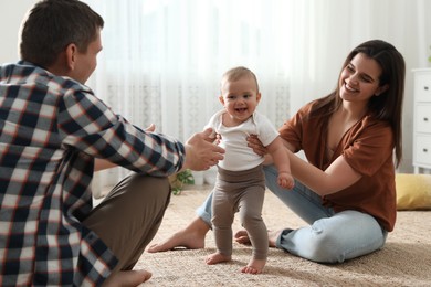 Parents supporting their baby daughter while she learning to walk at home