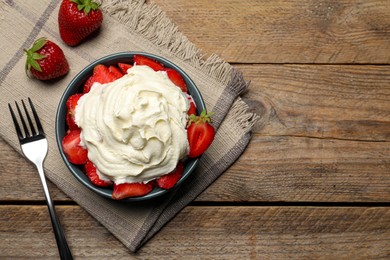 Photo of Bowl with delicious strawberries and whipped cream served on wooden table, flat lay. Space for text