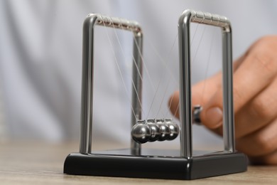 Photo of Man playing with Newton's cradle at table, closeup. Physics law of energy conservation