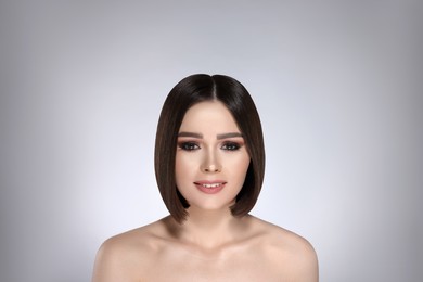 Portrait of pretty young woman with brown hair smiling on grey background