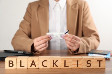 Photo of Word Blacklist of cubes and travel agent with toy airplane at wooden table, closeup