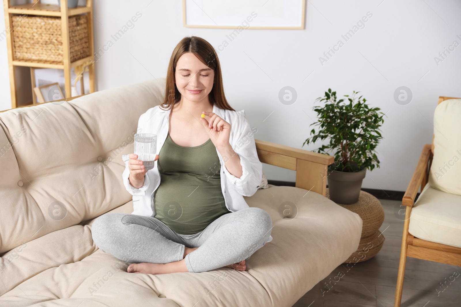 Photo of Beautiful pregnant woman holding pill and glass of water at home