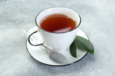 Aromatic tea in cup, spoon and green leaves on grey table