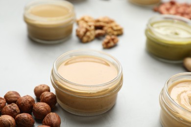 Photo of Different types of delicious nut butters and ingredients on light table, closeup