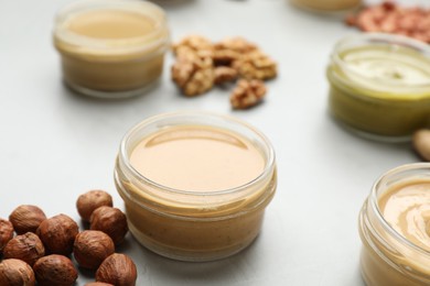 Different types of delicious nut butters and ingredients on light table, closeup