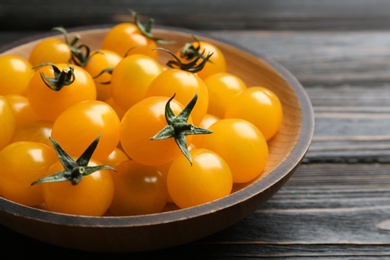 Photo of Ripe yellow tomatoes in bowl on dark wooden table, closeup