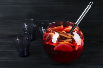 Photo of Bowl of delicious aromatic punch drink and glasses on black wooden table. Space for text