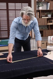 Photo of Professional tailor with measuring tape working at table in atelier