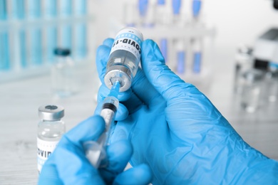 Doctor filling syringe with vaccine against Covid-19 at table, closeup