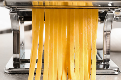 Photo of Pasta maker machine with dough on grey table, closeup