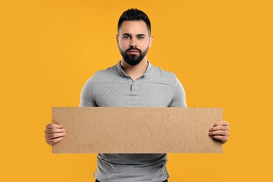Man holding blank cardboard banner on orange background, space for text