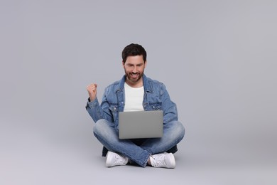 Emotional man with laptop on light grey background