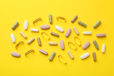 Different vitamin pills on yellow background, flat lay