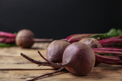 Photo of Fresh beets with leaves on wooden table against black background, closeup. Space for text