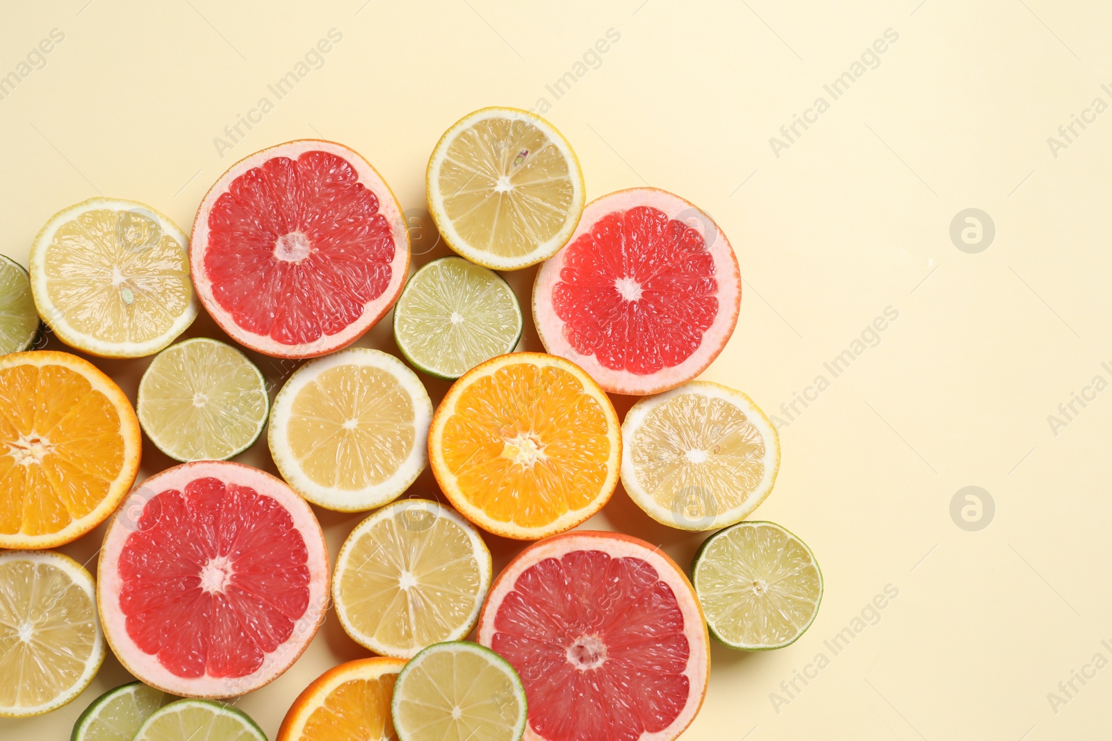 Photo of Different cut citrus fruits on beige table, flat lay. Space for text