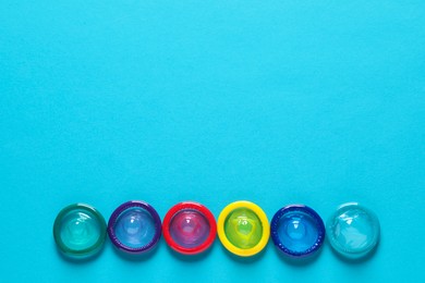 Colorful condoms on light blue background, flat lay. Space for text