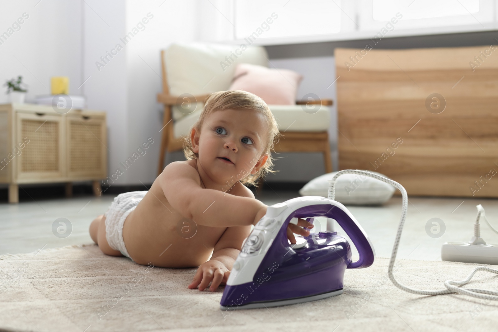 Photo of Cute baby playing with iron on floor at home. Dangerous situation