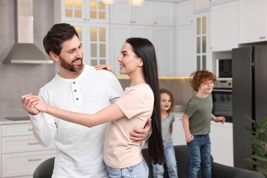 Photo of Happy family having fun at home. Couple dancing while children jumping on sofa