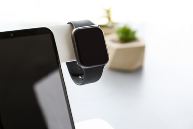 Photo of Stylish smart watch and phone charging with wireless pad against blurred background, closeup. Space for text