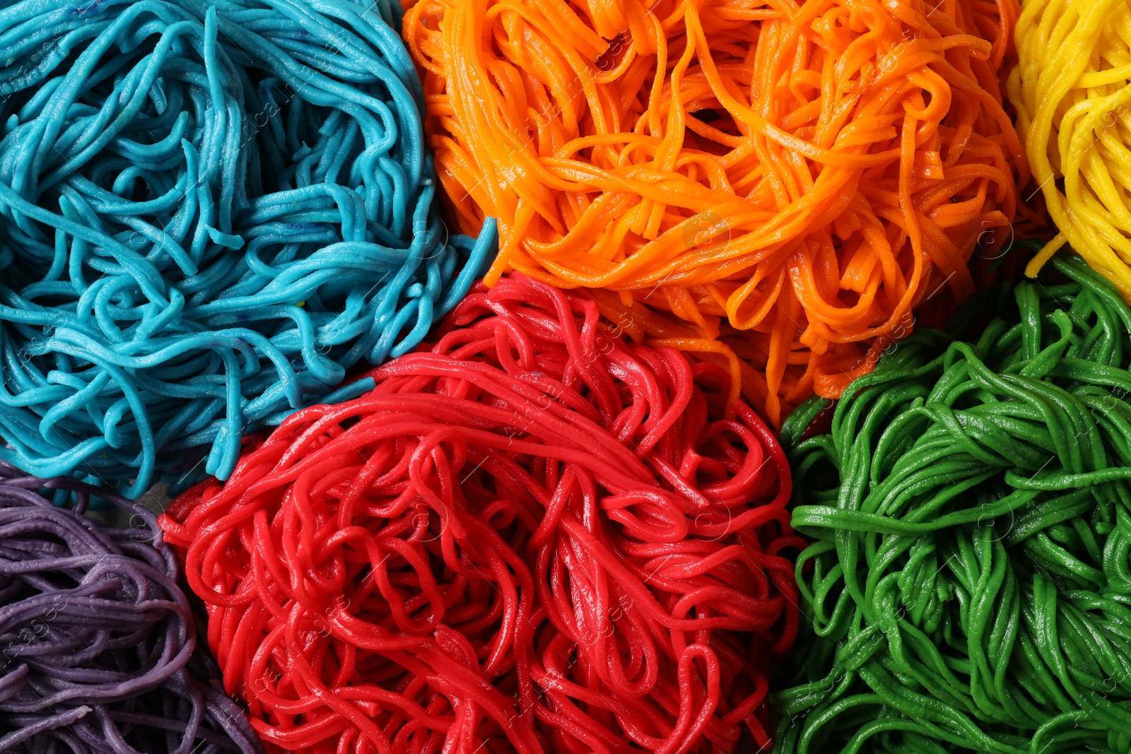 Photo of Rolled spaghetti painted with different food colorings as background, top view