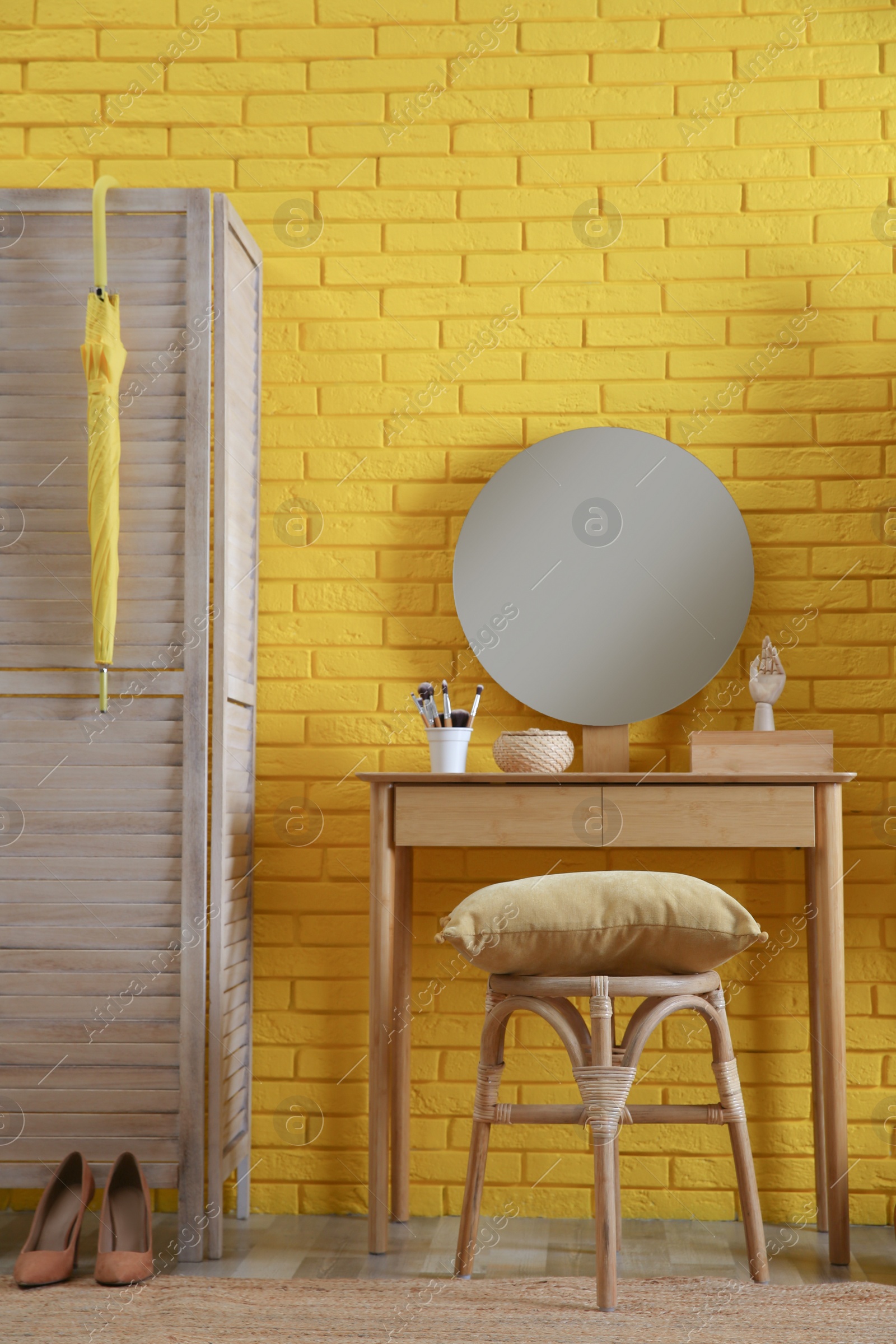 Photo of Wooden stool and dressing table near yellow brick wall indoors