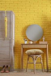 Photo of Wooden stool and dressing table near yellow brick wall indoors