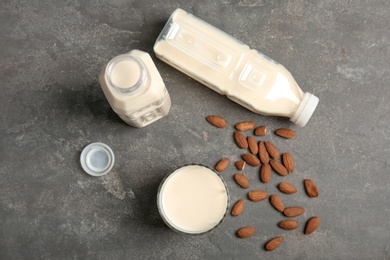 Glass and bottles with almond milk on grey background