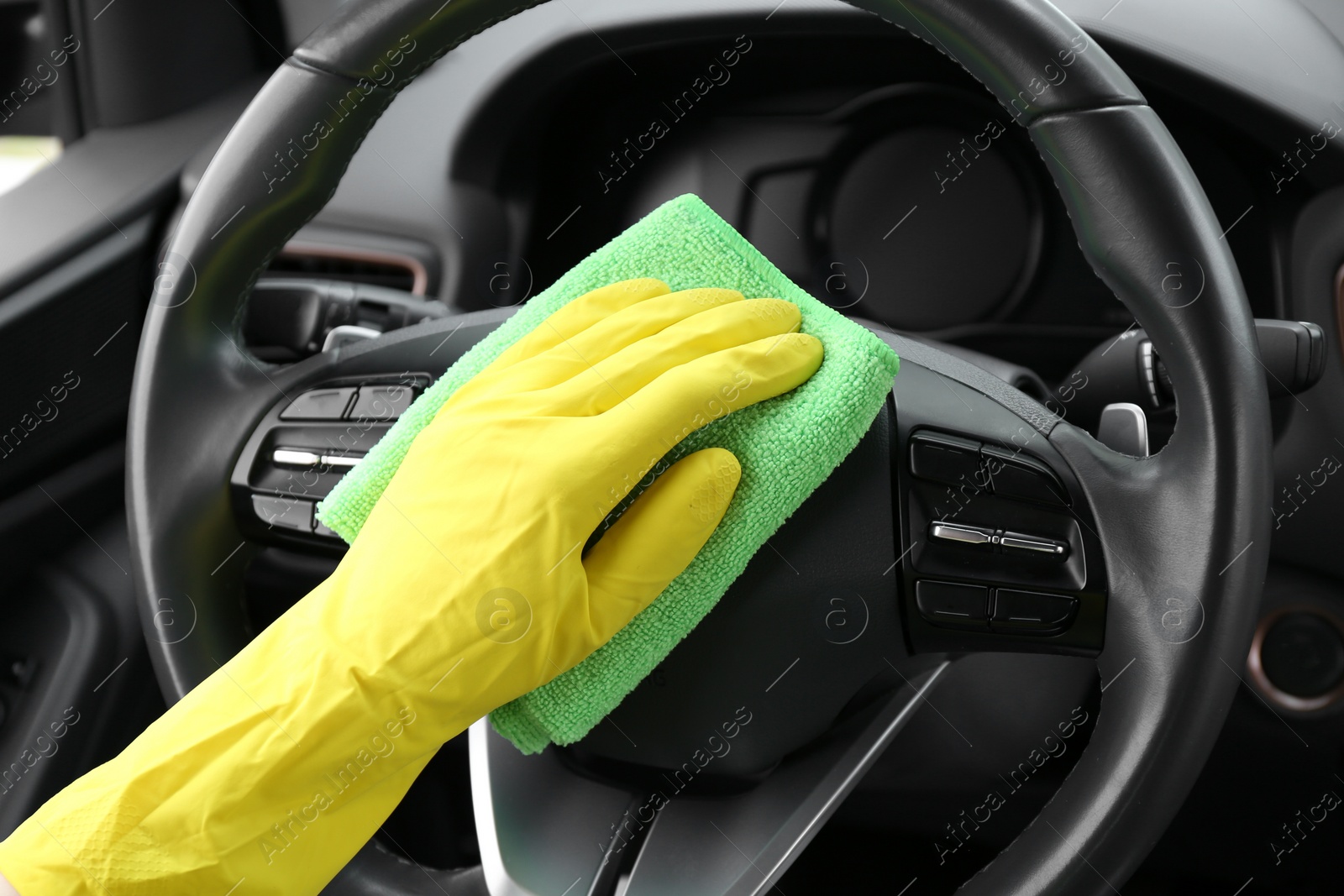 Photo of Woman cleaning steering wheel with rag in car, closeup