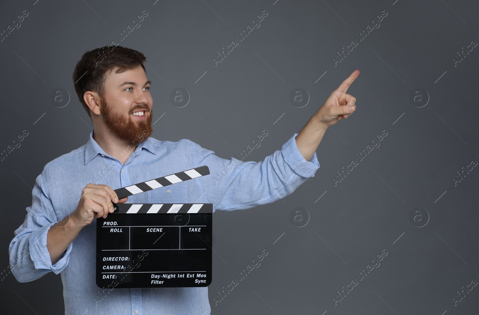 Photo of Making movie. Smiling man with clapperboard pointing at something on grey background