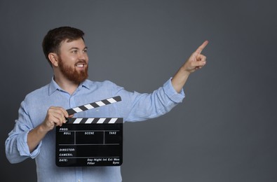 Making movie. Smiling man with clapperboard pointing at something on grey background