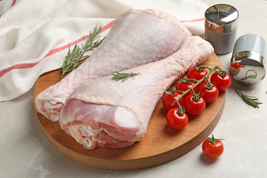 Board with raw turkey drumsticks, tomatoes and rosemary on table