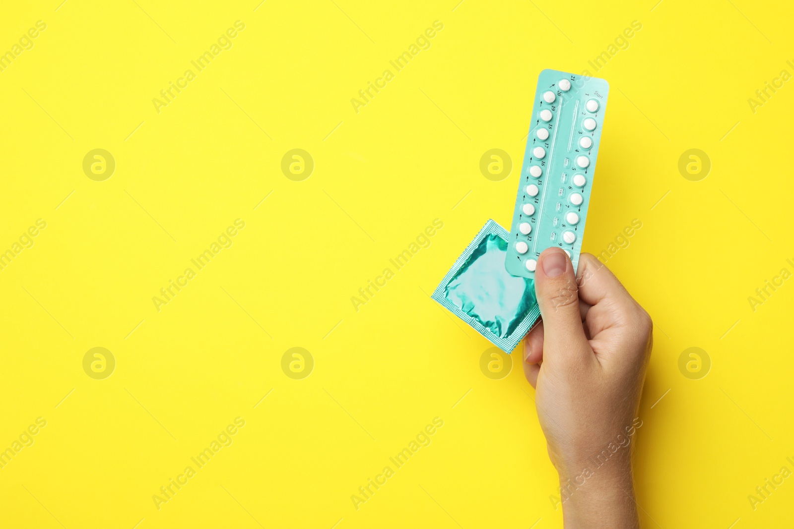 Photo of Woman holding condom and birth control pills on yellow background, top view with space for text. Safe sex