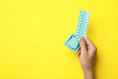 Photo of Woman holding condom and birth control pills on yellow background, top view with space for text. Safe sex