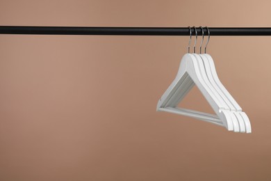 Photo of Empty clothes hangers on rack against light brown background. Space for text