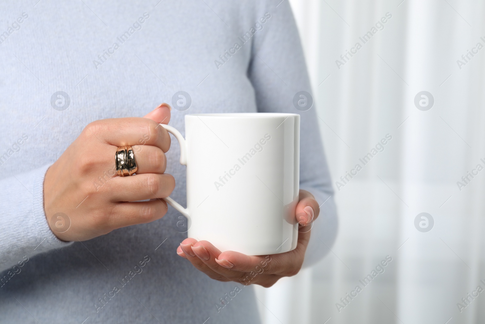 Photo of Woman holding white mug indoors, closeup. Mockup for design