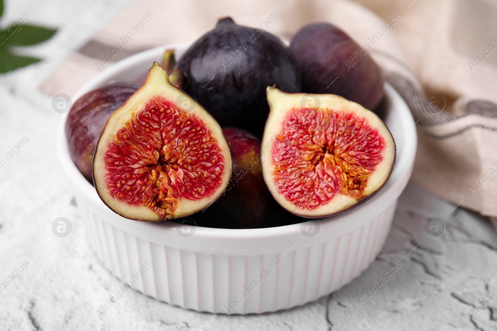 Photo of Bowl of tasty ripe figs on white textured table, closeup