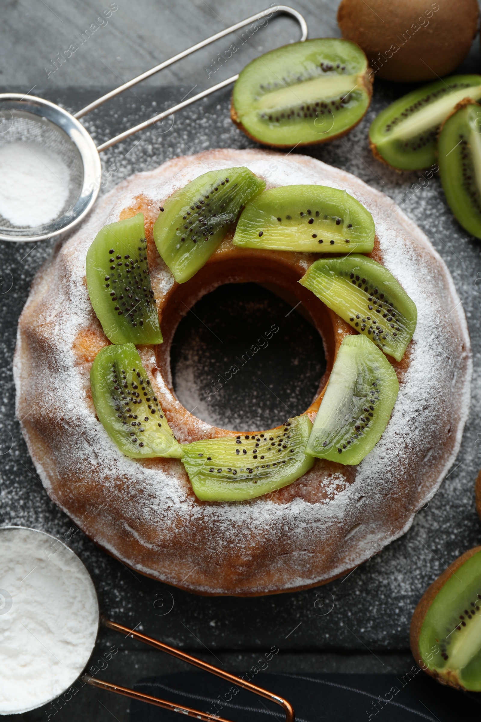 Photo of Homemade yogurt cake with kiwi and powdered sugar on black table, flat lay