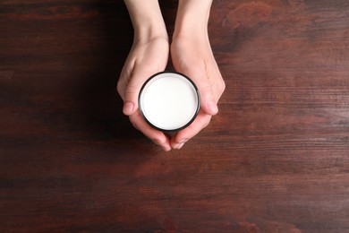 Photo of Woman holding glass of milk at wooden table, top view