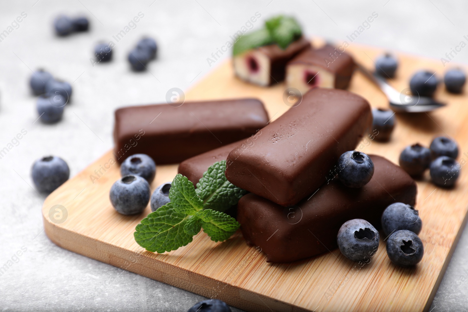 Photo of Delicious glazed curd snacks with fresh blueberries and mint on light grey table, closeup