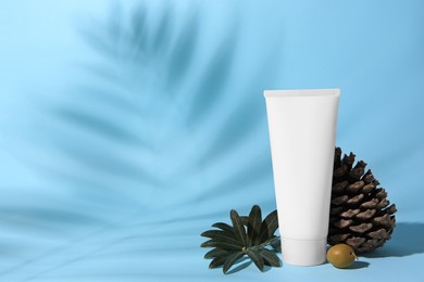 Photo of Tube of cream, olive and cone on light blue background, space for text. Cosmetic products