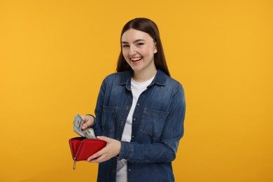 Happy woman putting money into wallet on orange background